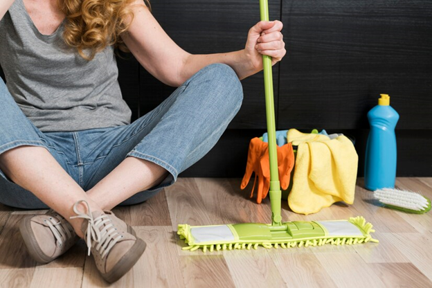 A lady sitting on the floor with a mop in hand